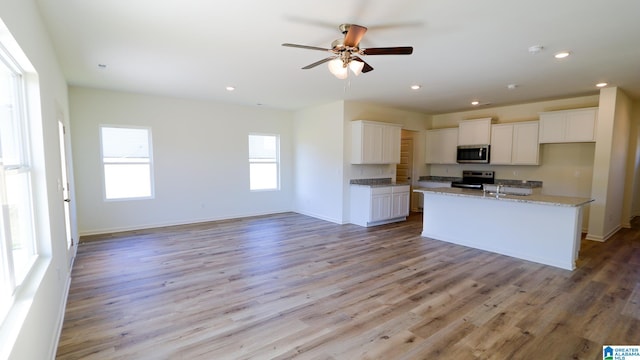 kitchen featuring stainless steel appliances, light stone counters, a kitchen island with sink, light hardwood / wood-style flooring, and white cabinets