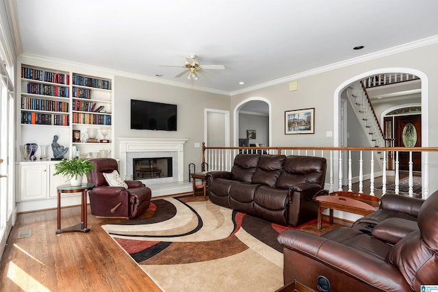 living room featuring ceiling fan, wood-type flooring, ornamental molding, and built in shelves