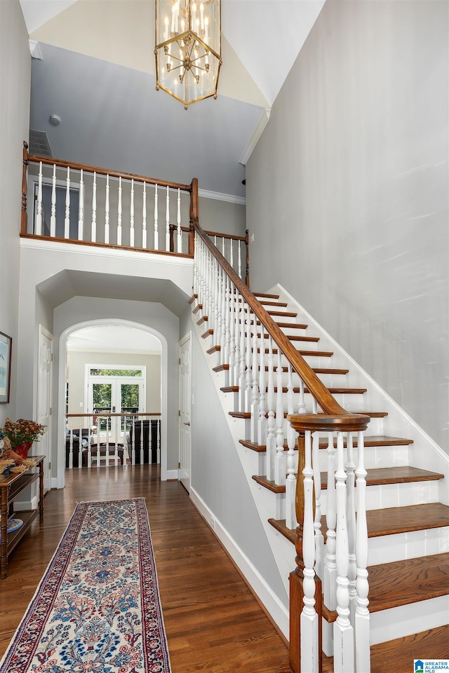 stairs with a notable chandelier, high vaulted ceiling, wood-type flooring, and crown molding