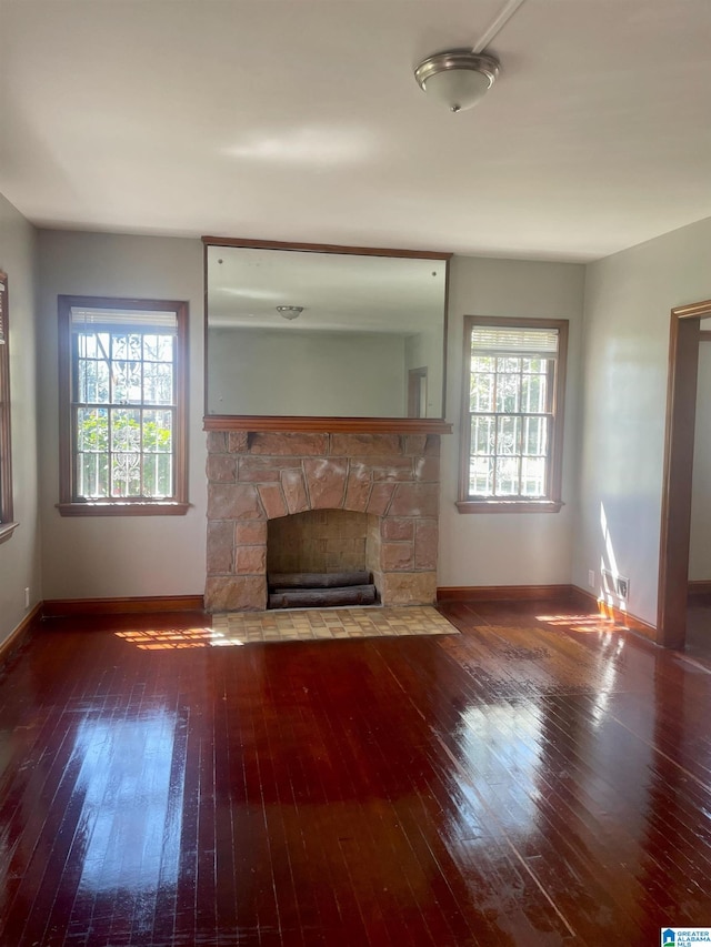 unfurnished living room with a stone fireplace, a healthy amount of sunlight, and dark wood-type flooring