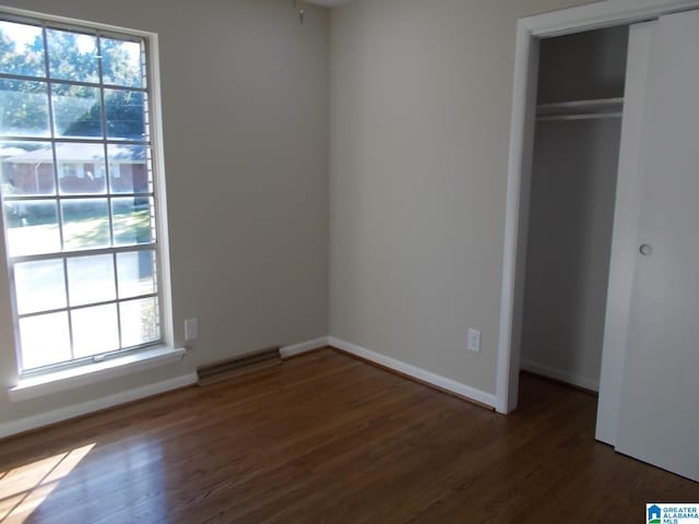 unfurnished bedroom with multiple windows, a closet, and dark hardwood / wood-style flooring