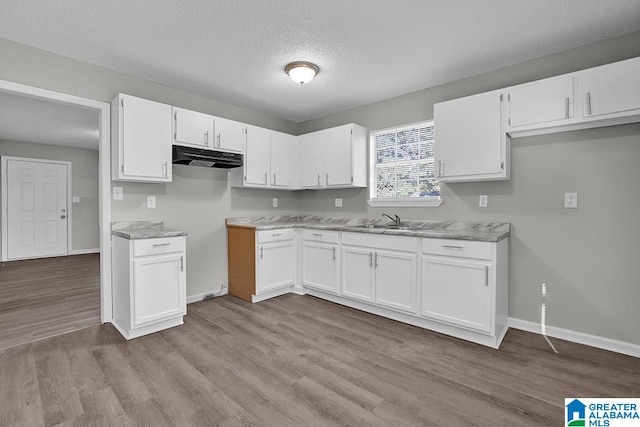 kitchen with light stone countertops, sink, light wood-type flooring, and white cabinets