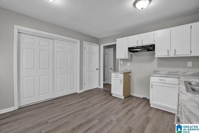 kitchen featuring sink, white cabinetry, light hardwood / wood-style flooring, and a textured ceiling