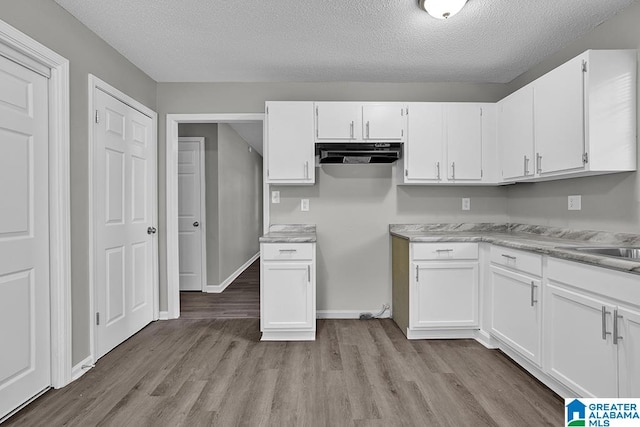 kitchen featuring white cabinets, a textured ceiling, and light wood-type flooring