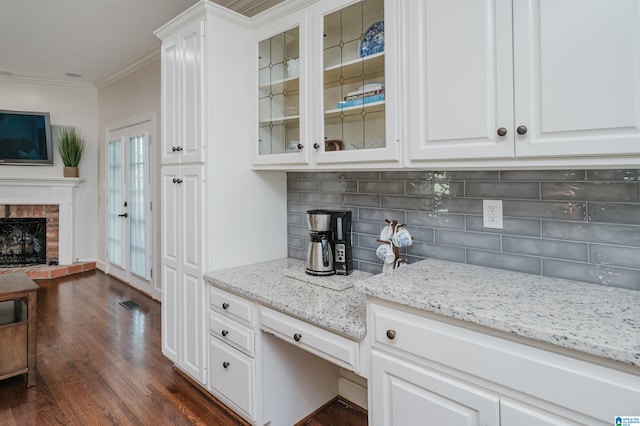 kitchen with backsplash, a brick fireplace, white cabinets, dark wood-type flooring, and ornamental molding