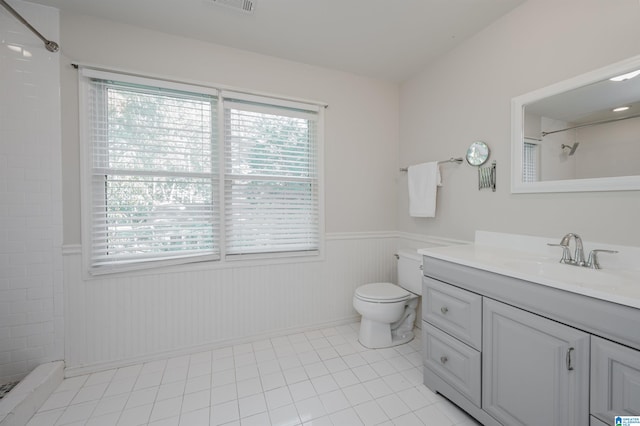 bathroom with toilet, a healthy amount of sunlight, vanity, and a tile shower