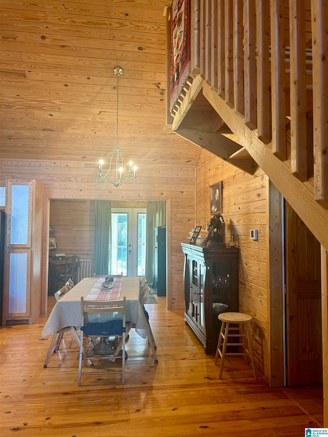 dining area with wooden walls, hardwood / wood-style flooring, and an inviting chandelier