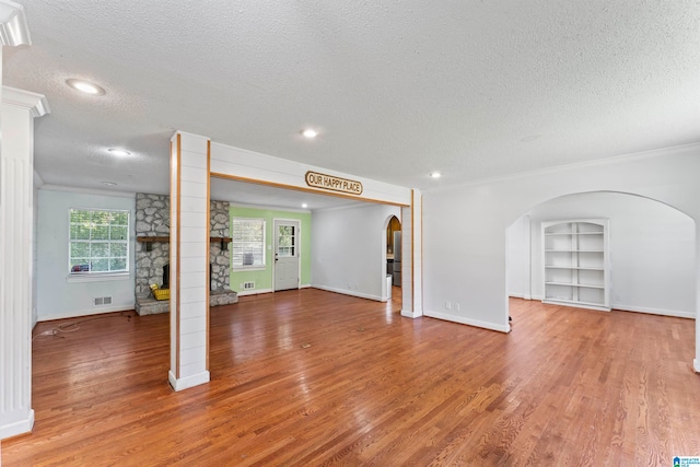 unfurnished living room featuring ornamental molding, hardwood / wood-style floors, a stone fireplace, and a textured ceiling