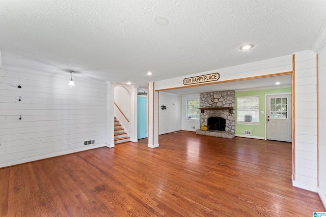 unfurnished living room with a textured ceiling, a stone fireplace, and hardwood / wood-style flooring