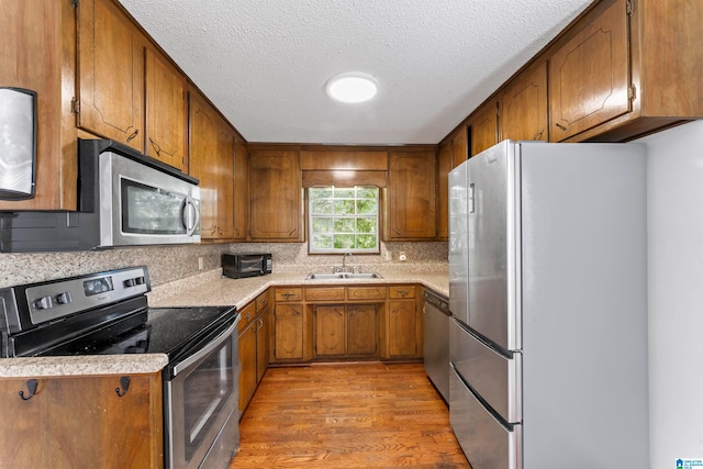 kitchen featuring tasteful backsplash, appliances with stainless steel finishes, a textured ceiling, light hardwood / wood-style flooring, and sink