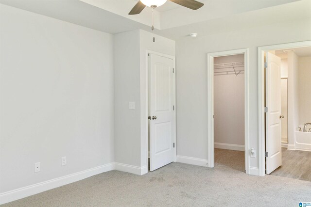 unfurnished bedroom featuring light carpet, a walk in closet, a closet, and ceiling fan