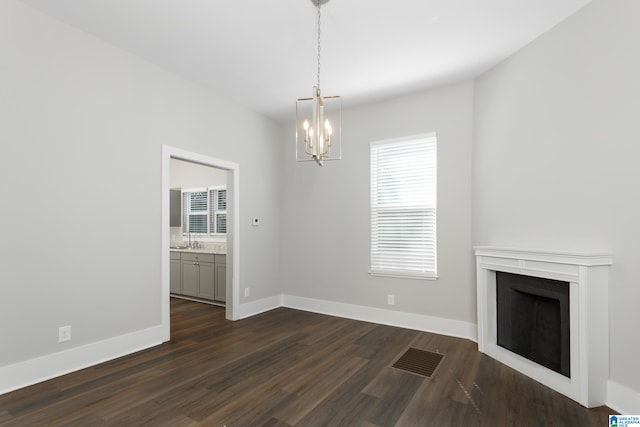 unfurnished living room with an inviting chandelier, dark hardwood / wood-style floors, and sink