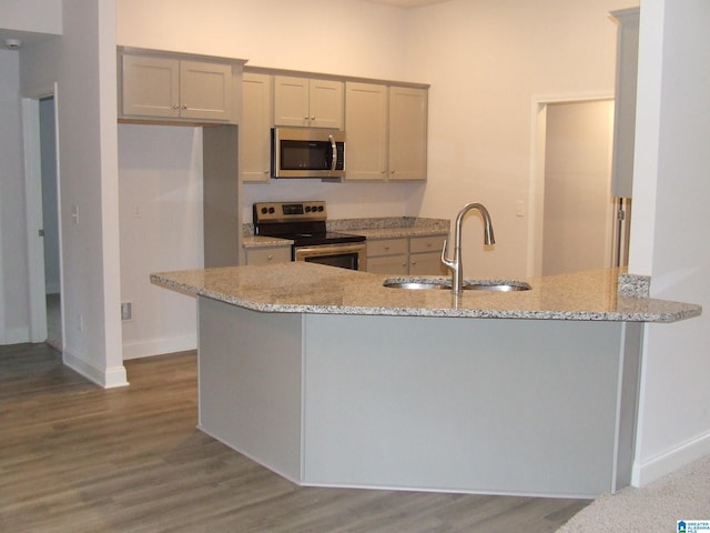 kitchen with kitchen peninsula, wood-type flooring, sink, light stone countertops, and appliances with stainless steel finishes