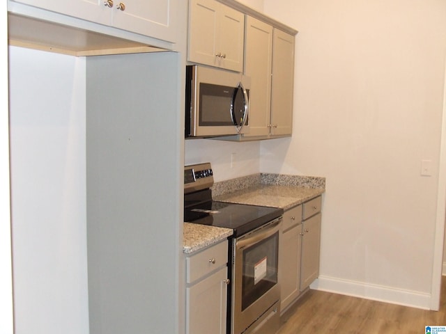 kitchen with stainless steel appliances, light stone countertops, and light hardwood / wood-style flooring