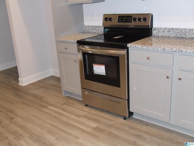 kitchen with white cabinetry, light stone countertops, electric range, and light wood-type flooring