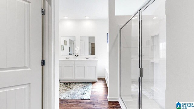 bathroom with wood finished floors, a sink, a shower stall, and double vanity