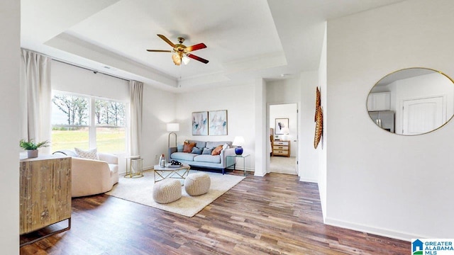 living room featuring ceiling fan, a tray ceiling, wood finished floors, and baseboards