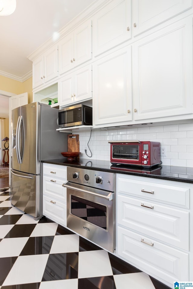 kitchen featuring white cabinets, ornamental molding, dark countertops, and appliances with stainless steel finishes