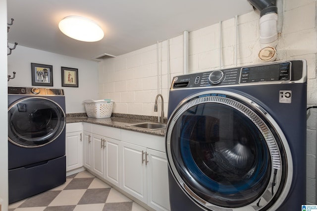 laundry room with a sink, cabinet space, concrete block wall, washer and dryer, and light floors