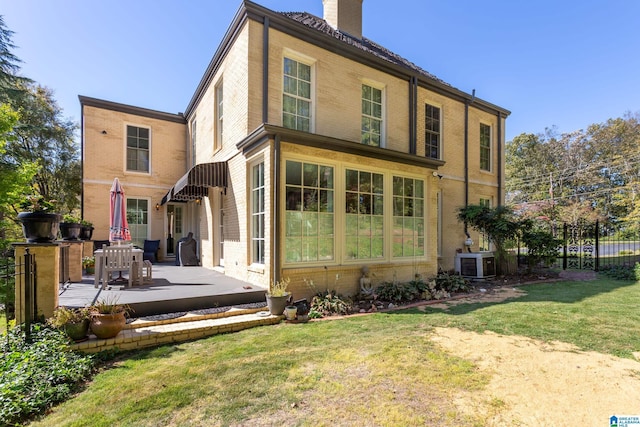 rear view of house featuring a chimney, brick siding, a patio area, cooling unit, and a lawn