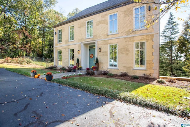 colonial-style house featuring a front lawn, fence, and brick siding