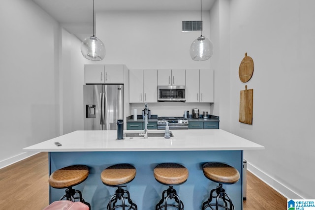 kitchen featuring light hardwood / wood-style floors, stainless steel appliances, hanging light fixtures, and an island with sink