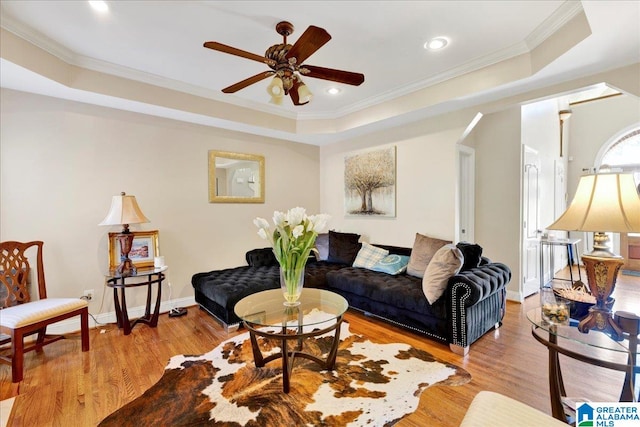 living room with ceiling fan, a raised ceiling, ornamental molding, and light wood-type flooring