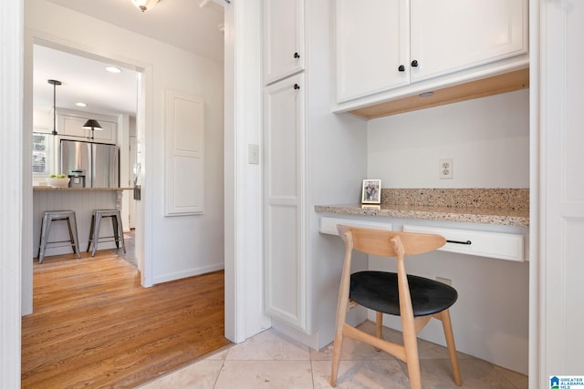 kitchen with a breakfast bar area, light stone countertops, stainless steel fridge with ice dispenser, white cabinets, and light hardwood / wood-style floors