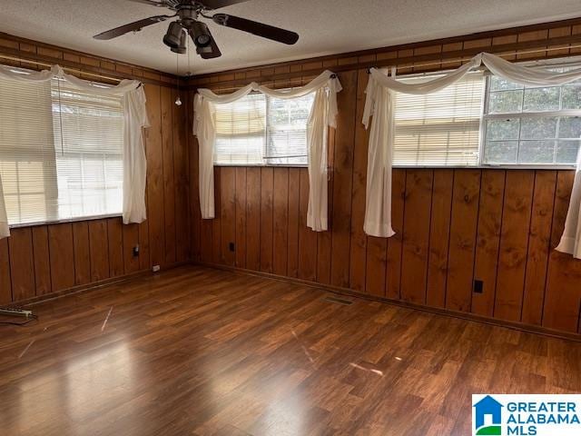 empty room with dark hardwood / wood-style floors, wood walls, a textured ceiling, and ceiling fan