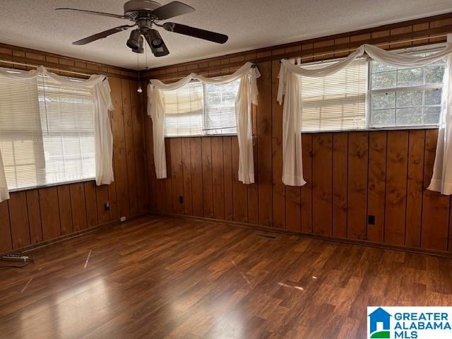 spare room with a textured ceiling, dark hardwood / wood-style flooring, ceiling fan, and wood walls