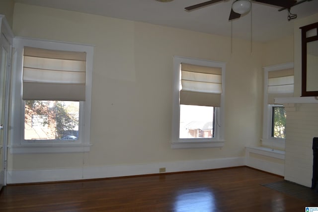 spare room with dark hardwood / wood-style flooring, a brick fireplace, plenty of natural light, and ceiling fan