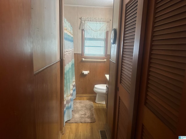 bathroom with a textured ceiling, wood-type flooring, toilet, and wood walls