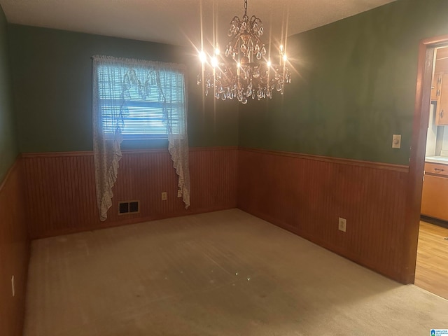 unfurnished room featuring wood walls, a chandelier, and light colored carpet