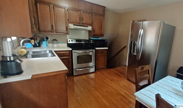 kitchen with appliances with stainless steel finishes, kitchen peninsula, sink, and light wood-type flooring