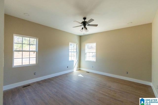 empty room featuring wood finished floors, a ceiling fan, visible vents, and baseboards