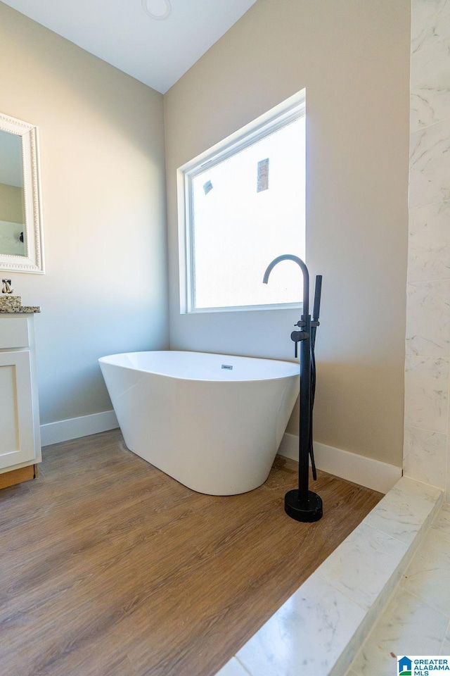 bathroom featuring vanity, a freestanding tub, wood finished floors, and baseboards