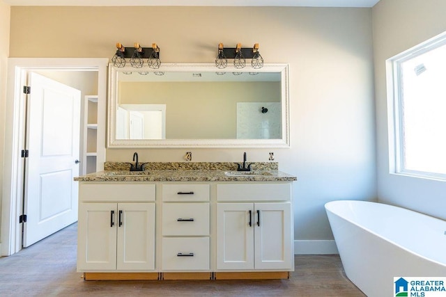 bathroom with a soaking tub, wood finished floors, double vanity, and a sink