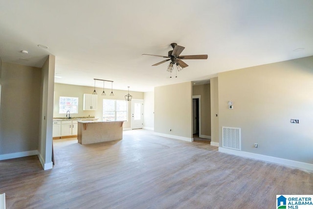 unfurnished living room with light wood-type flooring, visible vents, a sink, baseboards, and ceiling fan