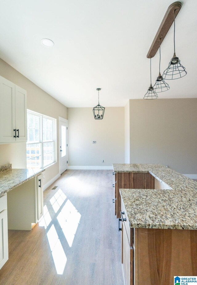 kitchen with light wood-style flooring, light stone counters, decorative light fixtures, white cabinetry, and baseboards