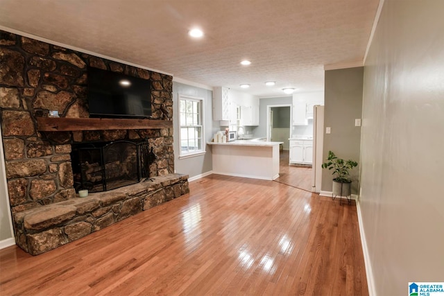 living room featuring a stone fireplace, light hardwood / wood-style flooring, a textured ceiling, and crown molding