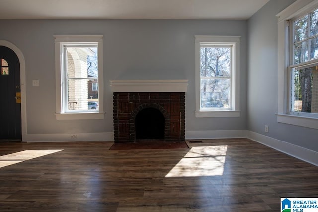 unfurnished living room with a healthy amount of sunlight, dark hardwood / wood-style flooring, and a brick fireplace