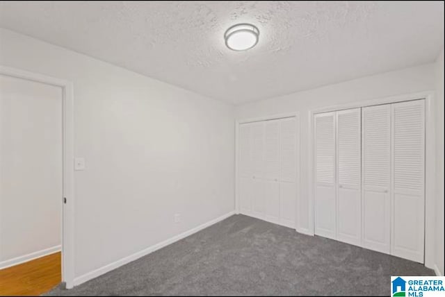 unfurnished bedroom featuring a textured ceiling, two closets, and dark carpet