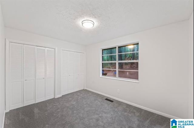 unfurnished bedroom featuring a textured ceiling, multiple closets, and dark carpet