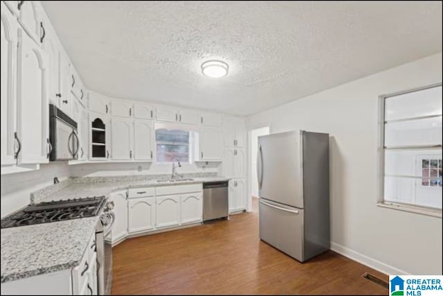 kitchen featuring wood-type flooring, stainless steel appliances, a textured ceiling, sink, and white cabinets