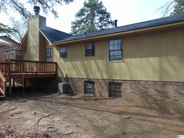 back of property featuring a deck, brick siding, central AC, and a chimney