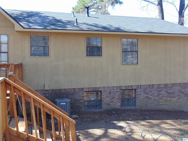 view of side of home featuring brick siding, central AC unit, a shingled roof, and stairs