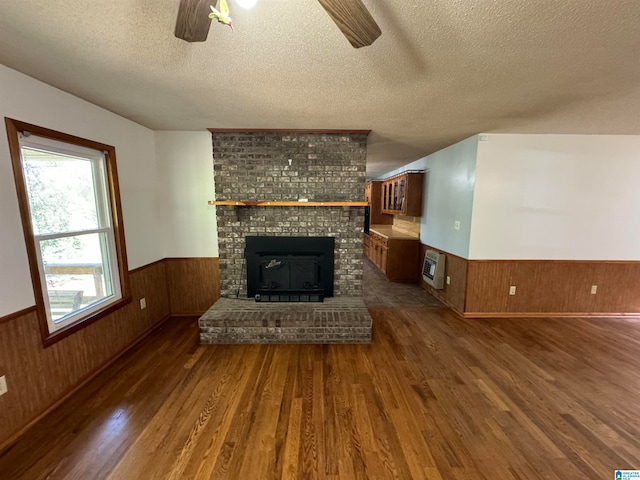 unfurnished living room with wood walls, a textured ceiling, dark wood-type flooring, and ceiling fan