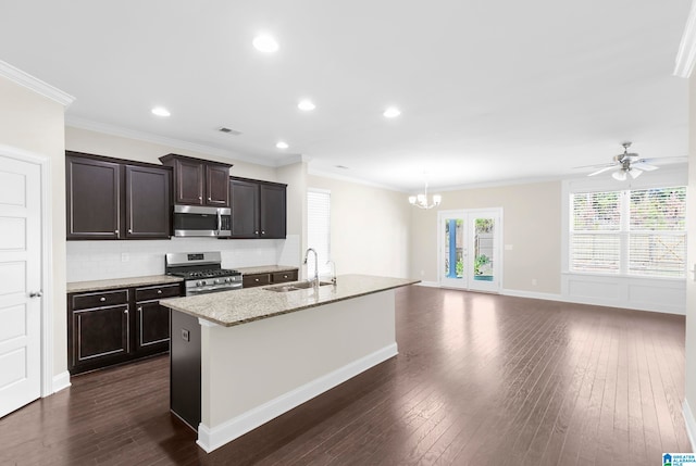 kitchen featuring appliances with stainless steel finishes, ceiling fan with notable chandelier, dark wood-type flooring, ornamental molding, and a kitchen island with sink