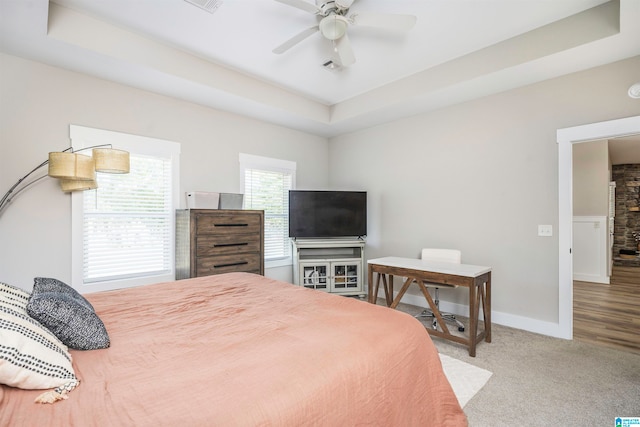 bedroom with light colored carpet, a tray ceiling, and ceiling fan