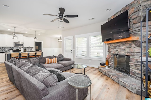 living room with light hardwood / wood-style floors, a stone fireplace, and ceiling fan